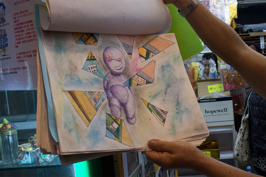 老板罗先生翻开一张由街坊送赠的画作，寓意领展破坏小店的生存空间。