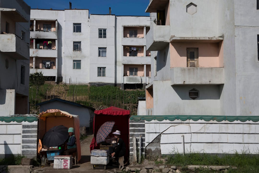 清津郊区，朝鲜妇女坐在一幢住宅前的小卖车摆卖。