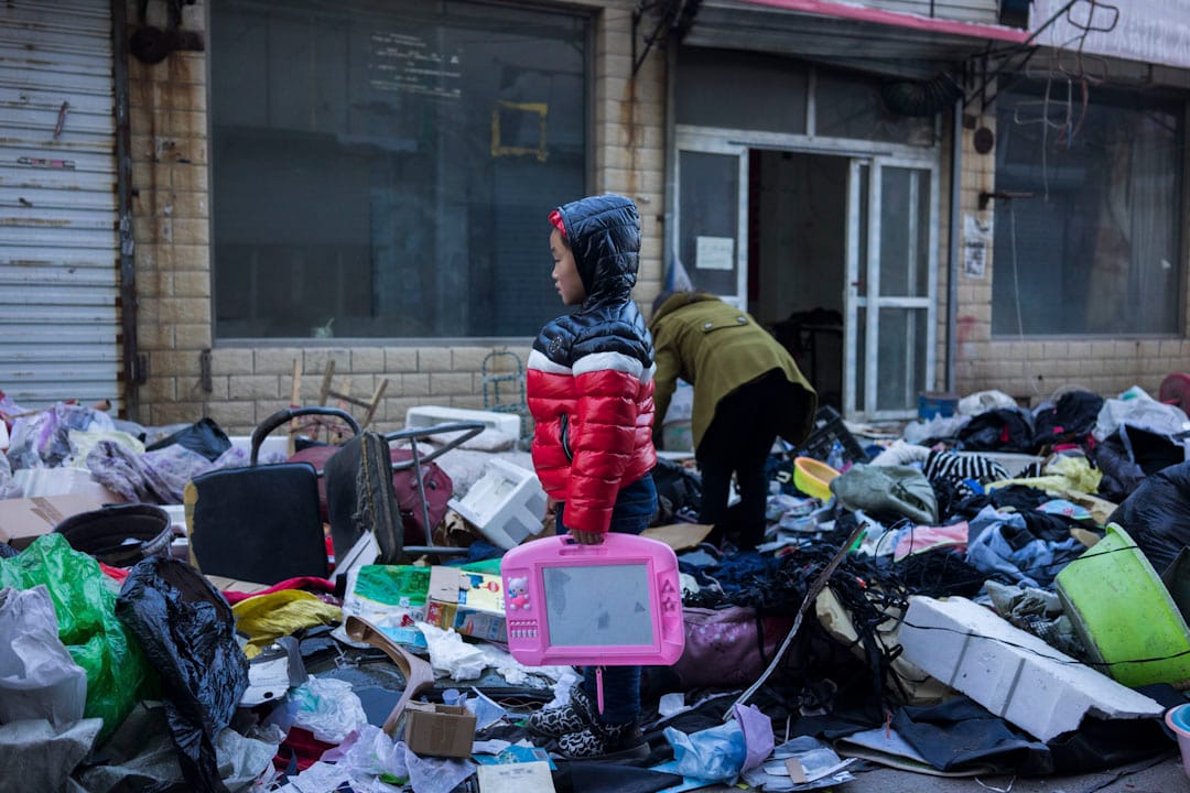 2017年11月26日下午，新建村街道上一個小孩和家人在堆滿廢棄物的街道上尋找能用的物品。
