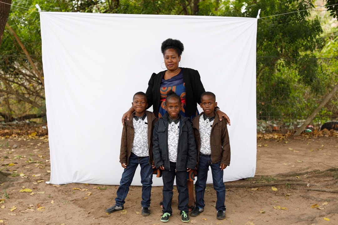 43歲的Nomathandazo Madlala和她的三胞胎兒子站在白布前。