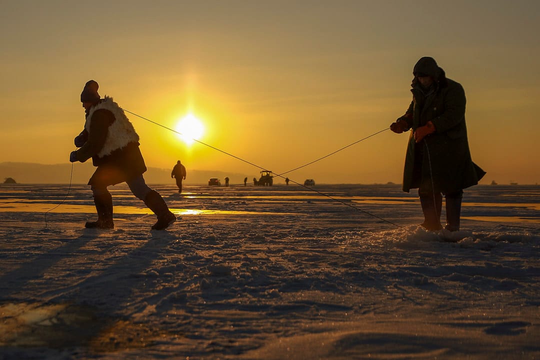 日出前，渔民扛著钢绳向前拉。