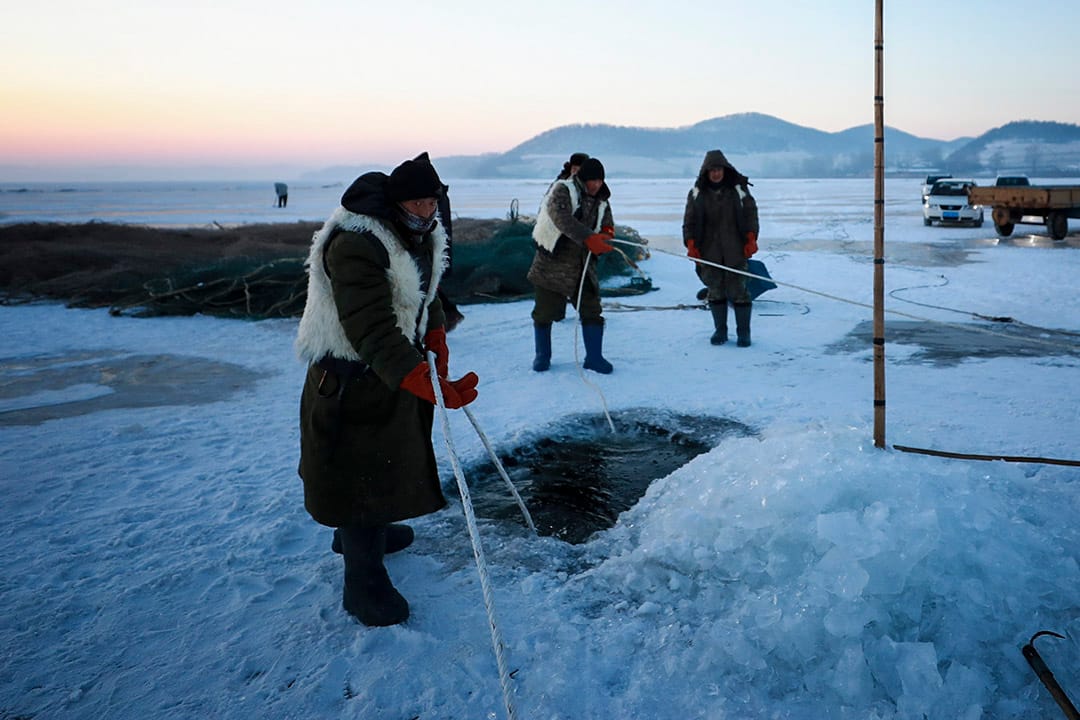 渔民在冰上钻开一个洞，将渔网放入水中。