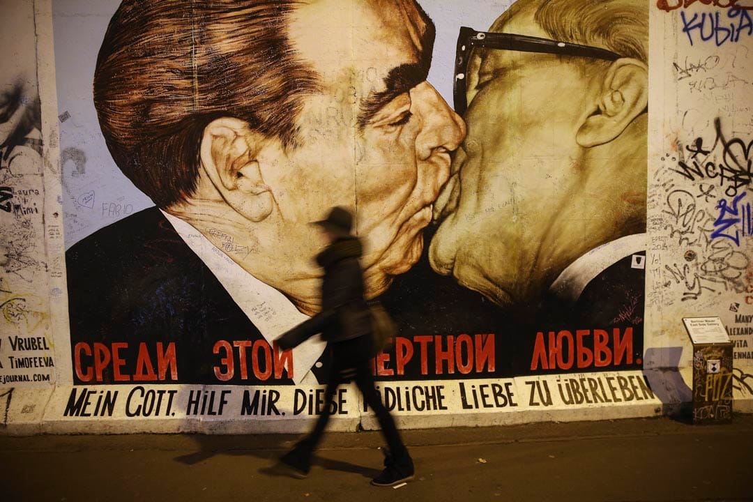 一位遊客走過一幅柏林圖牆一幅壁畫，展示前蘇聯領導人勃烈日涅夫親吻前東德共產黨領袖何內克。
