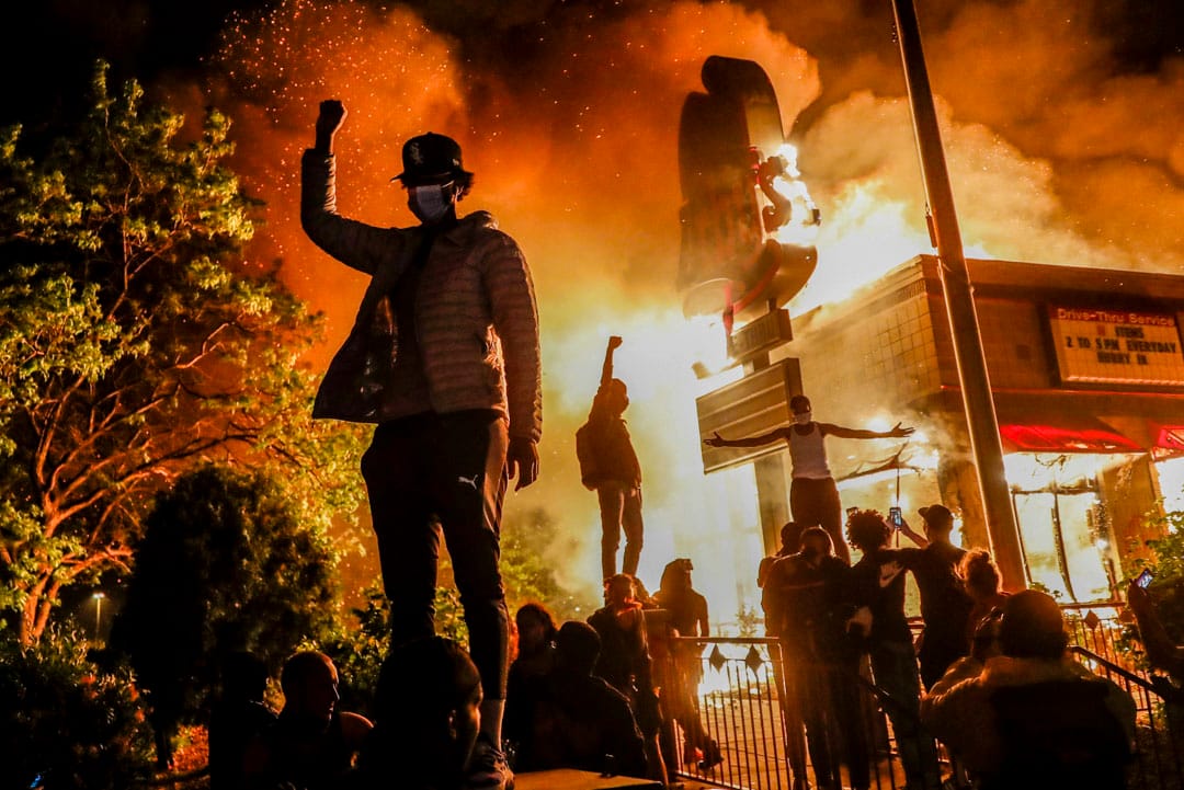 2020年5月29日，美國明尼蘇達州阿波利斯市一位示威者在焚燒中的快餐店外示威。數天前美國黑人喬治·佛洛伊德（George Floyd）在美國中西部明尼蘇達州的明尼阿波利斯市（Minneapolis）被白人警官用膝蓋壓制頸部8分鐘，弗洛伊德其後身亡。觸發了美國近年來圍繞種族問題的最大規模抗議浪潮。