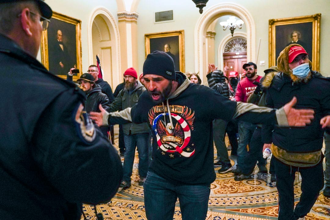 2021年1月6日，美國國會，一名特朗普支持者在參議院會議廳外向一名國會警察示意。
