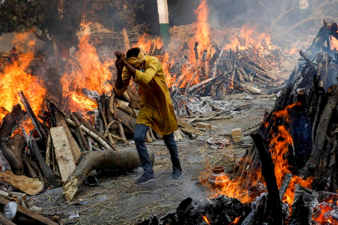 2021年4月26日，印度新德里的一个火葬场，一名男子穿过燃烧中的火堆。