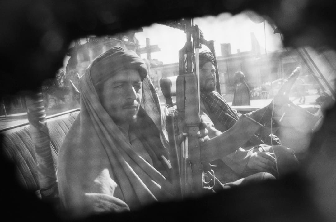 摄影师从罩袍下拍摄数名持枪的塔利班战士。