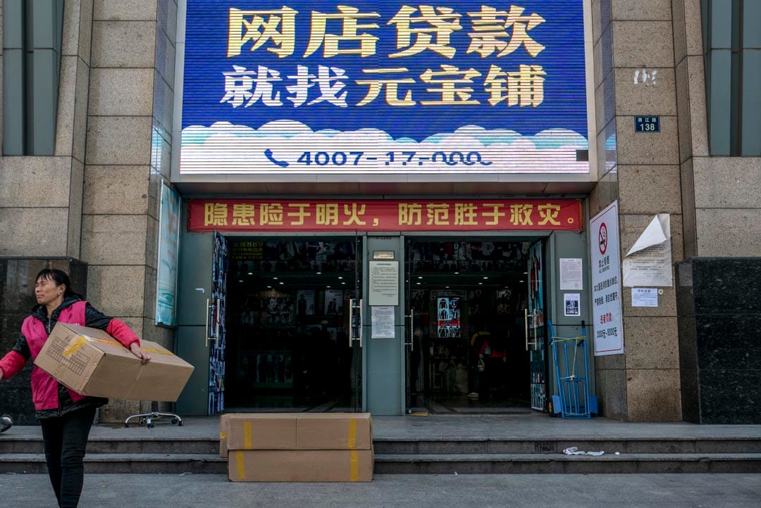2015年11月27日﹐大楼门口贴着向淘宝店主借贷的大广告,前有一名女士正运载着货物 。