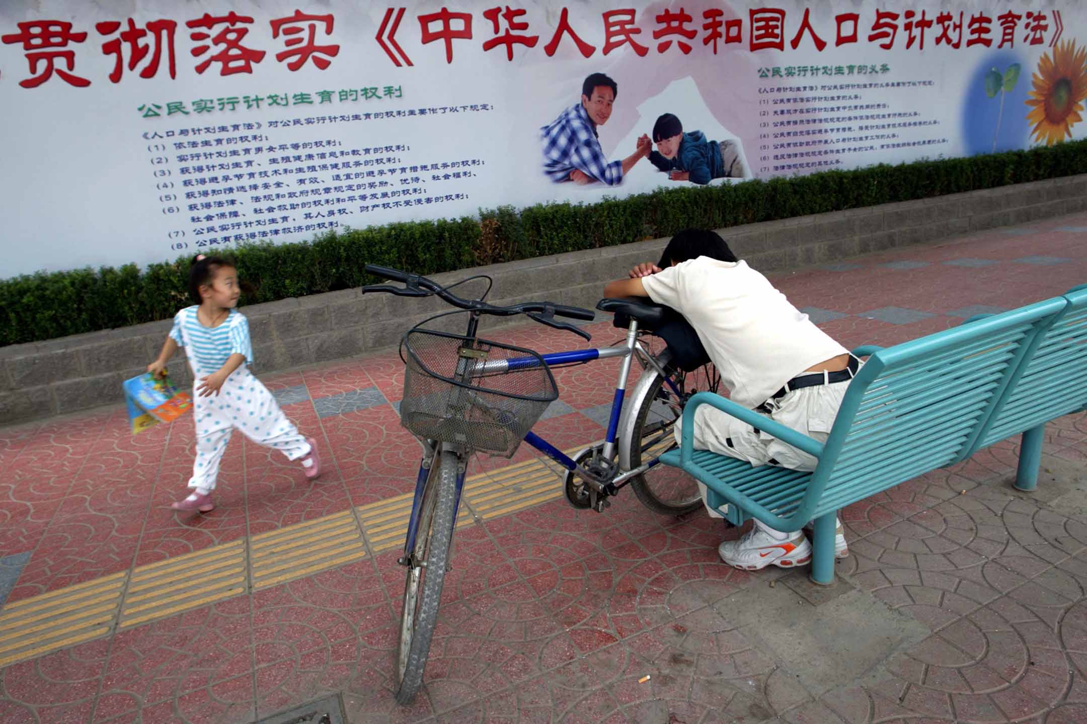 2002年8月30日，北京，一個女孩在計劃生育的宣傳牌前玩耍。