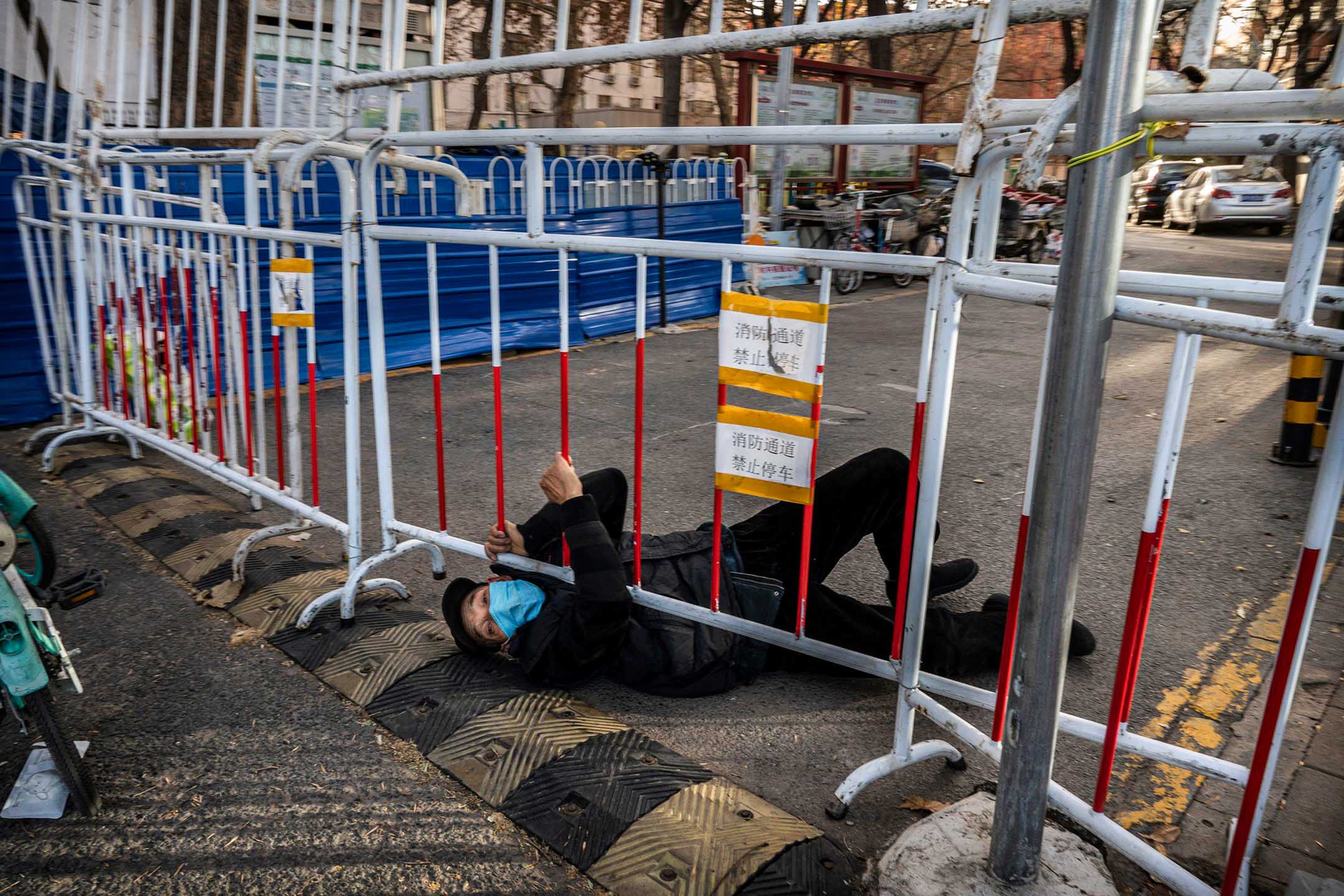 2022年12月3日，北京，一名男子企图在铁栏下突破封锁区。