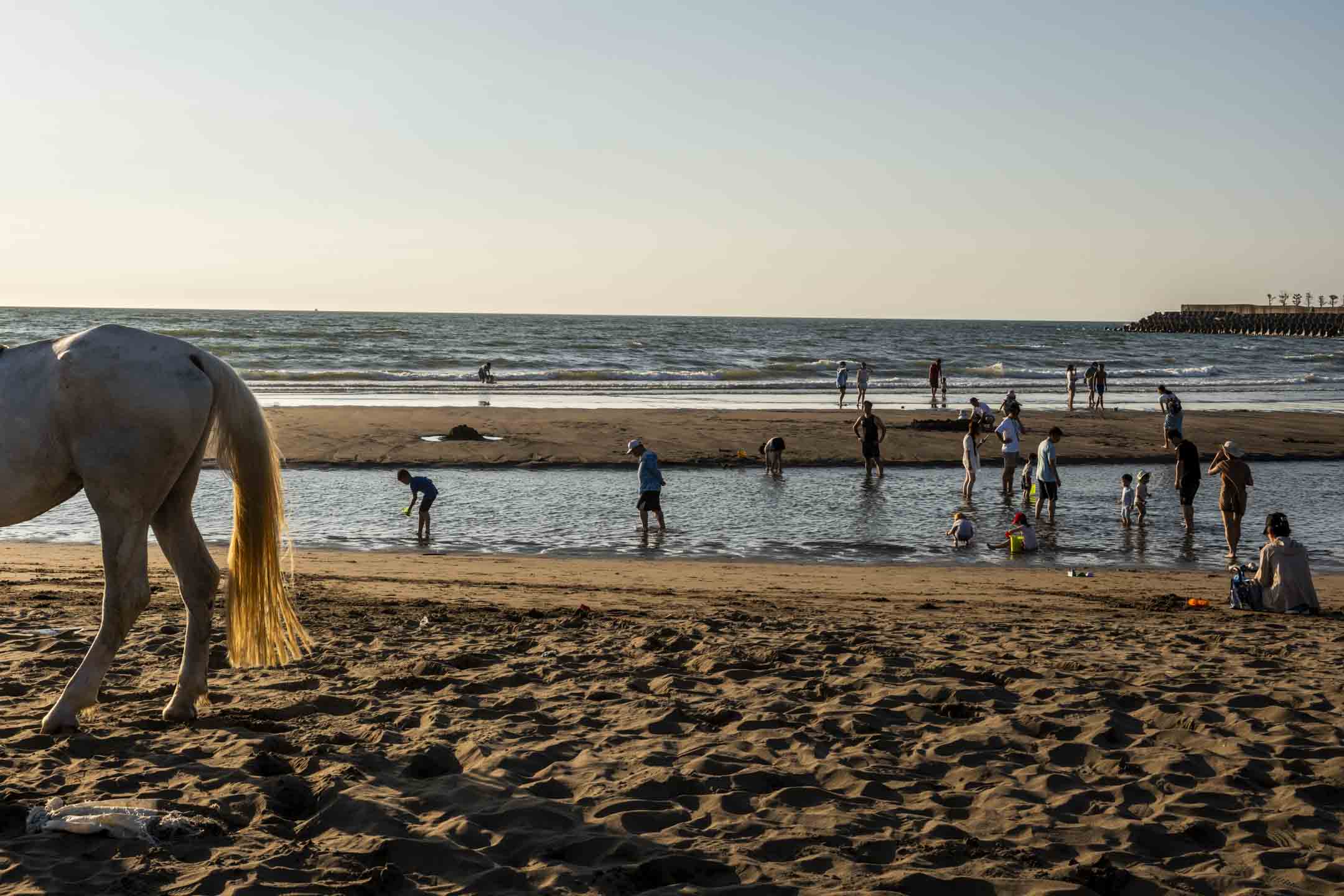 2023年7月9日,台湾淡水,人们在炎热的天气下在沙滩上玩水。摄:林振东/端传媒