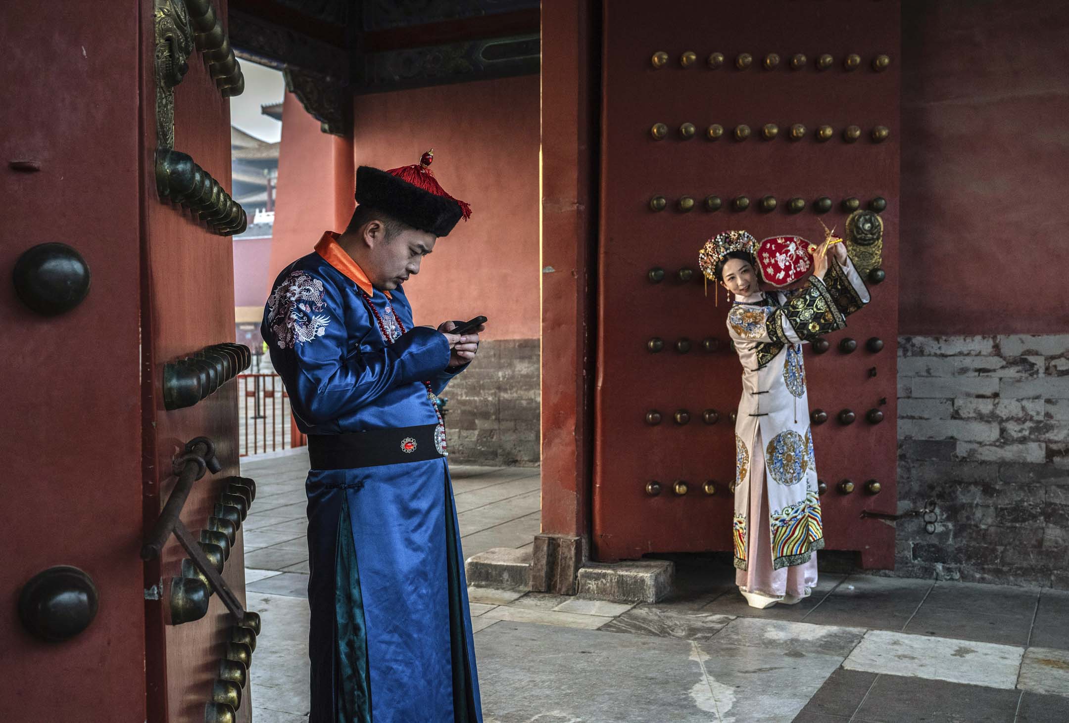 2023年11月21日,中國北京,兩名穿上清朝服裝的男女在紫禁城,男子看著自己的手機,女子則在擺姿勢拍照。攝:Kevin Frayer/Getty Images