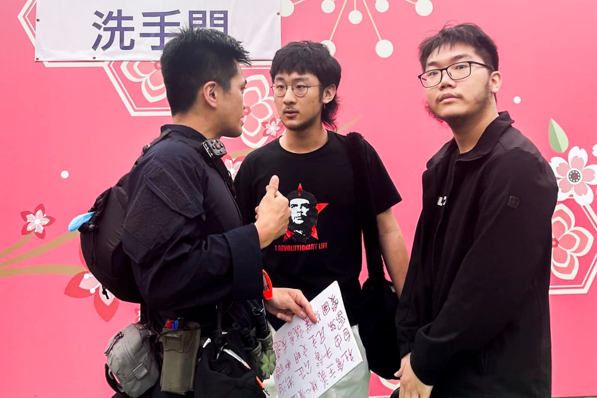 2024年6月4日，维园家乡情市集，有两名男子手持写上“社会主义核心价值观”等字眼的标语。其中一名男子被在场保安包围抬离维园，警察将他带上警车。