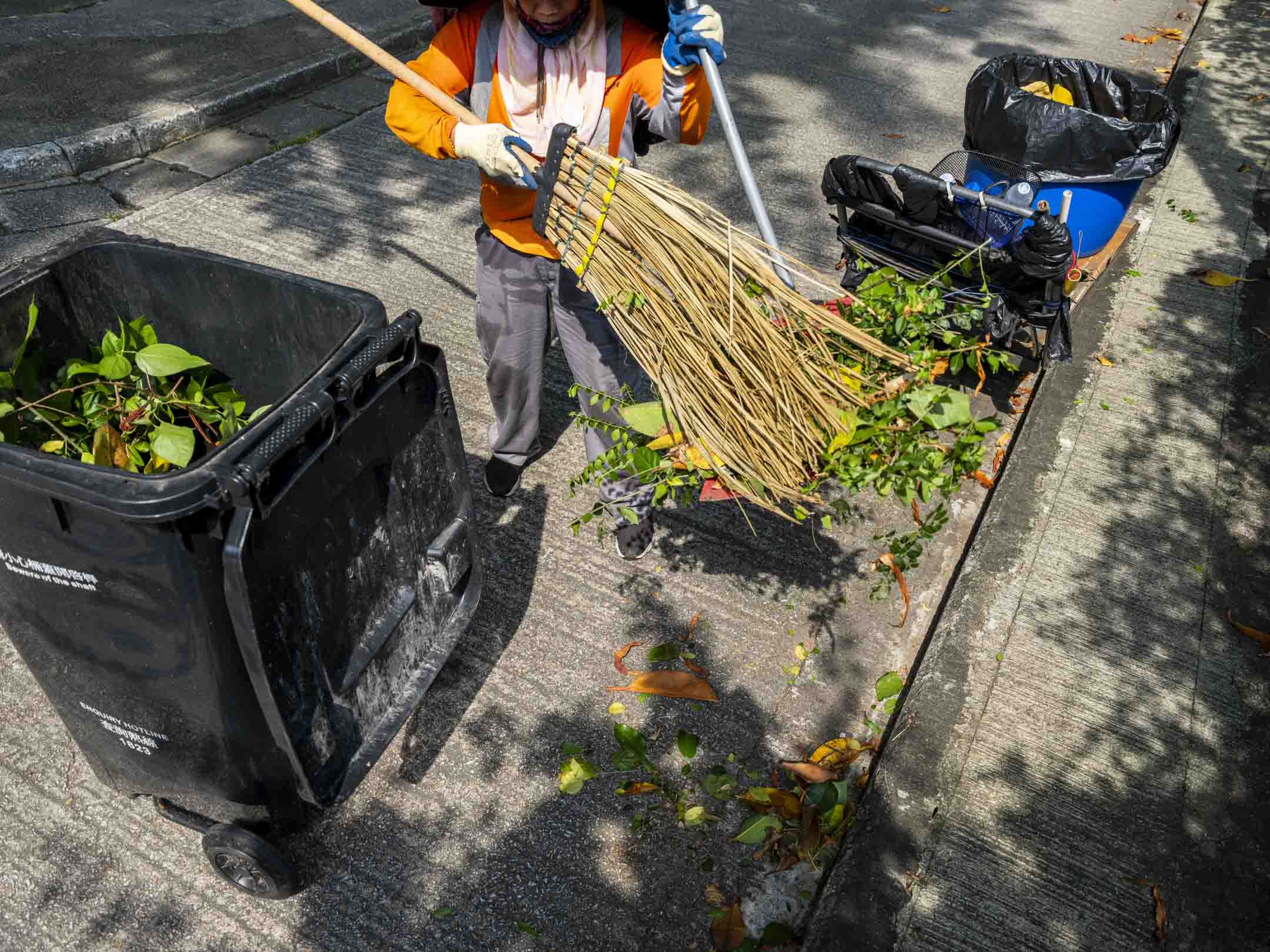 清潔工人蓮姐頭戴自製的遮陽帽,包著頭巾在烈日下掃街。攝:林振東/端傳媒