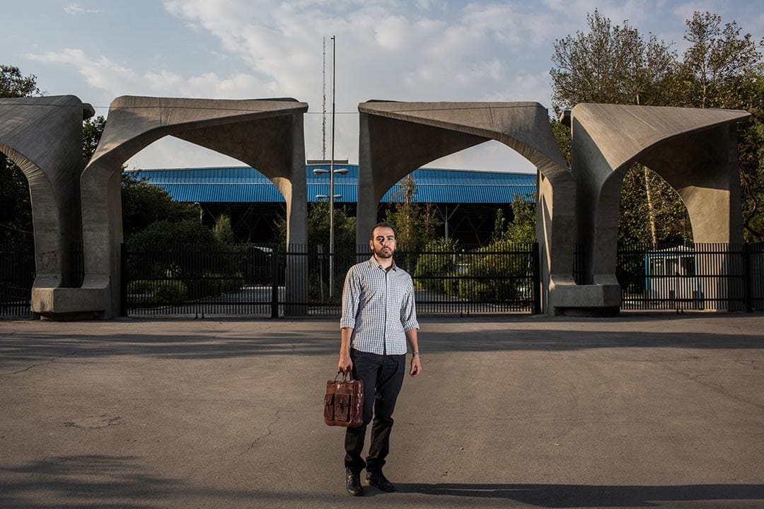 Mohammad Ali Mir Bagheri，三十歲的德黑蘭大學哲學系博士生，站於大學入口處。德黑蘭大學是伊朗其中一間「常春藤盟校」。為了維持生計，他正在做多份兼職。但他無法找到與他學科有關的工作。攝：Arash Khamooshi/端傳媒