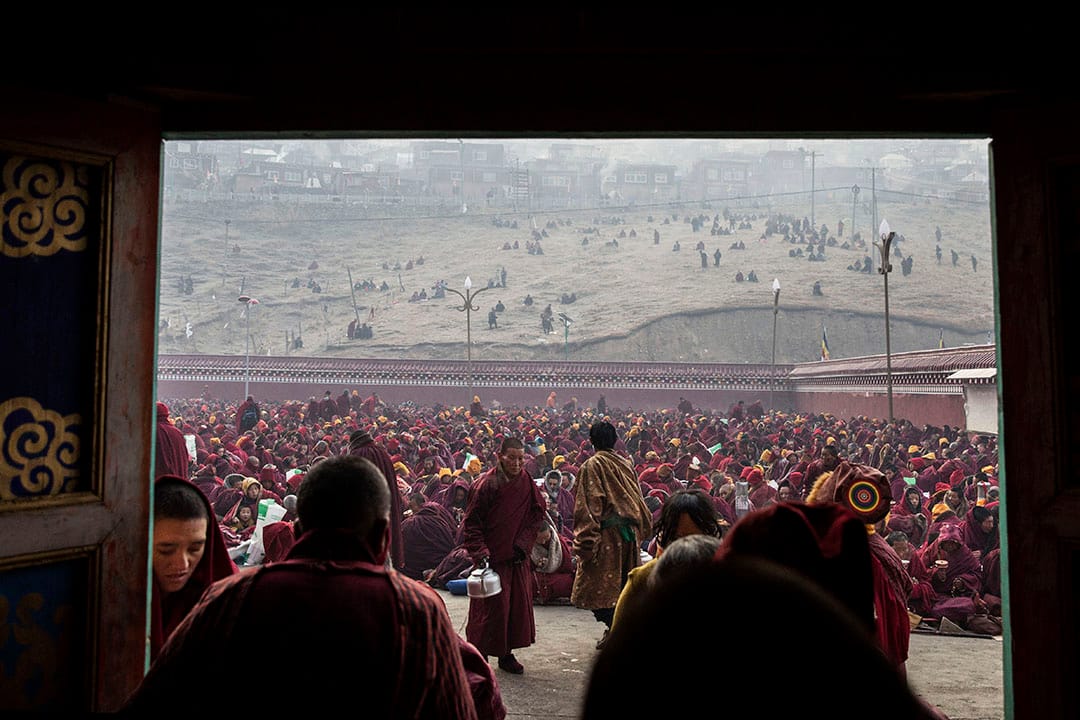 在色達喇榮五明佛學院內，一些喇嘛在喝茶，背後坐著成千的喇嘛。攝：Kevin Frayer/Getty Images
