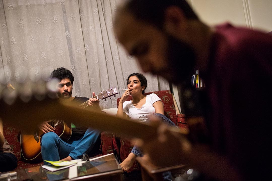 Melika，22歲，一個德黑蘭的蠟染學生。她正在聆聽她的畫家朋友 Mojtaba 和 Erfan 彈奏結他。攝：Arash Khamooshi/端傳媒