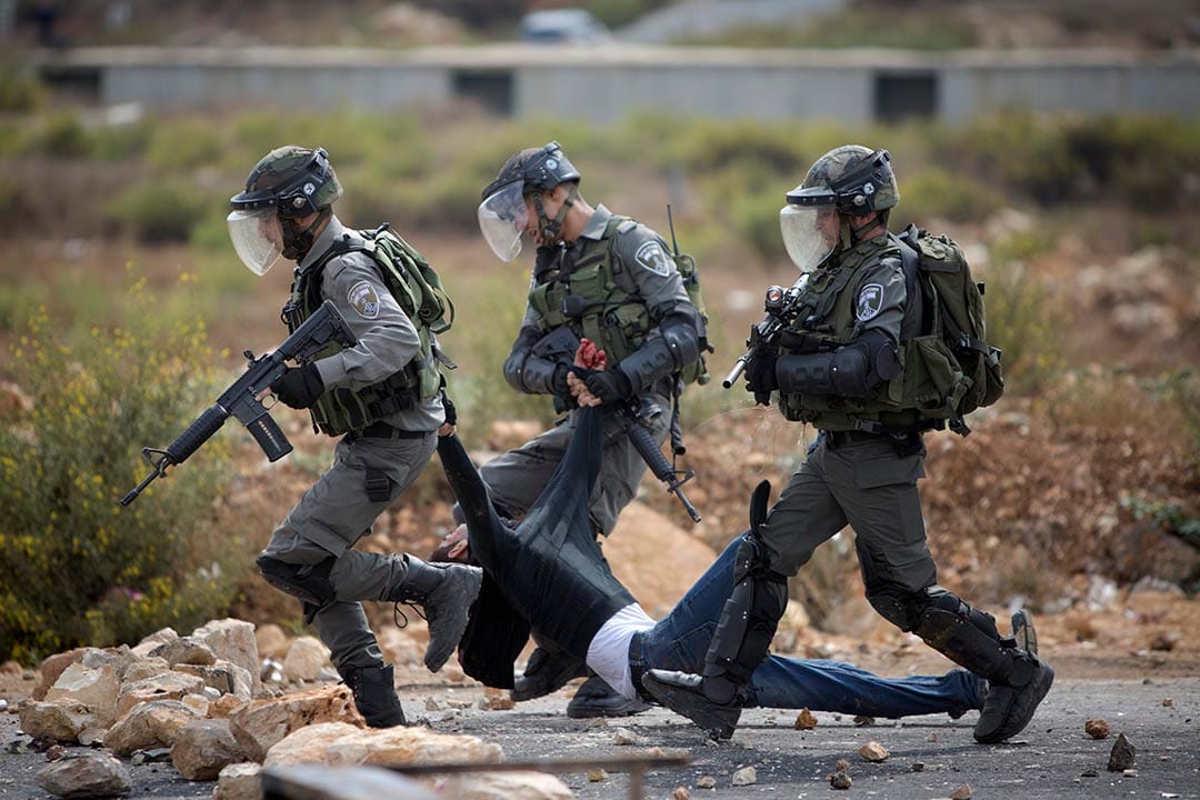 2015年10月7日，约旦河西岸城市拉姆安拉， 以色列军人在冲突中搀扶一名受伤的巴勒斯坦男子。摄：Majdi Mohammed/AP