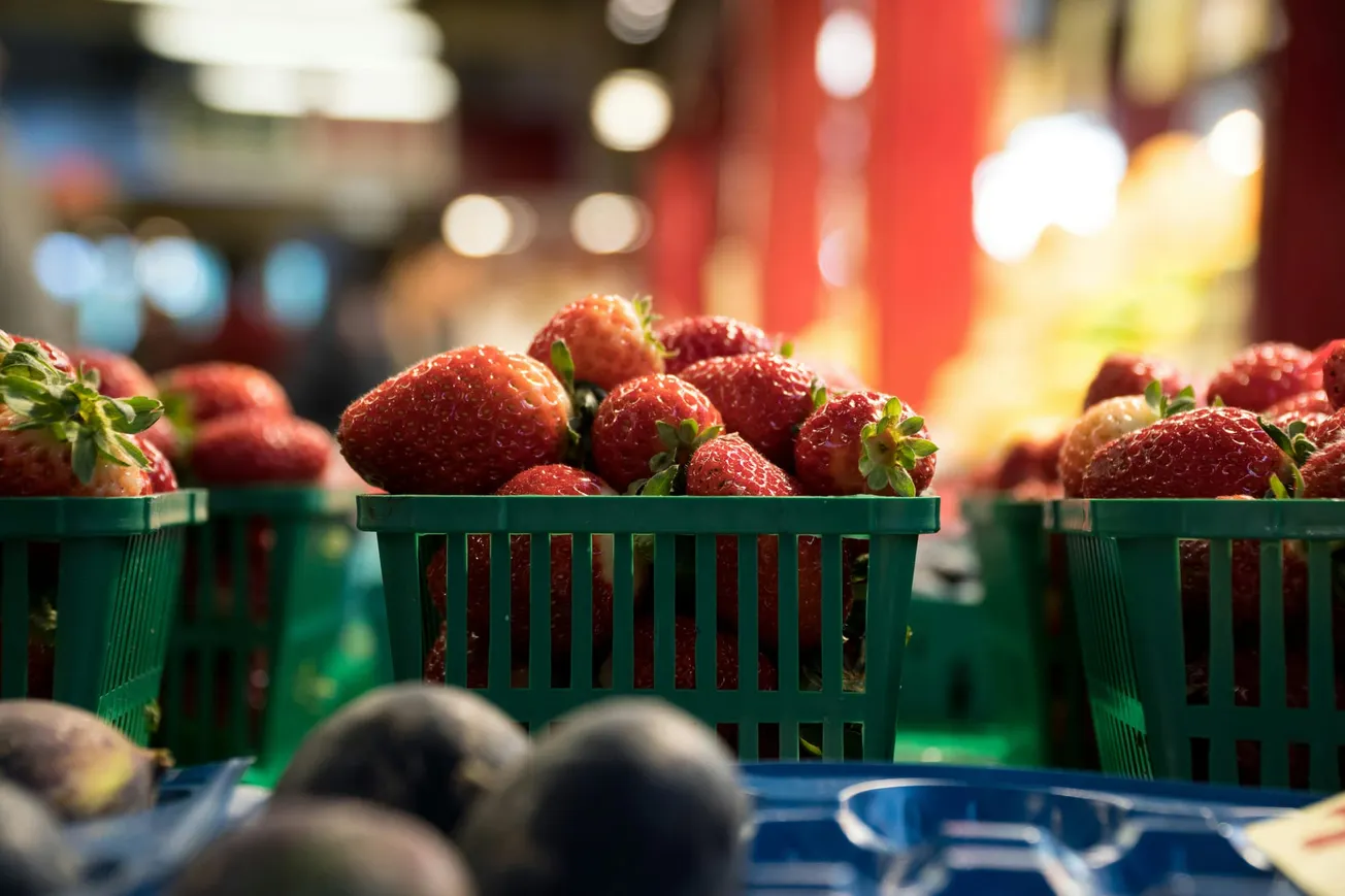 Close-up of ripe strawberries in green baskets at a market stall. Bright red berries are in focus.