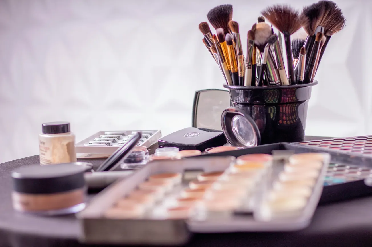 A variety of makeup tools and products, including brushes, palettes, and powders, are arranged on a table.