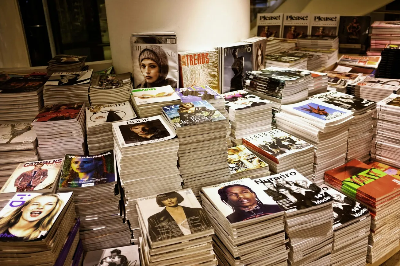 Stacks of fashion magazines are neatly arranged on a store table, showcasing colorful covers with striking images.