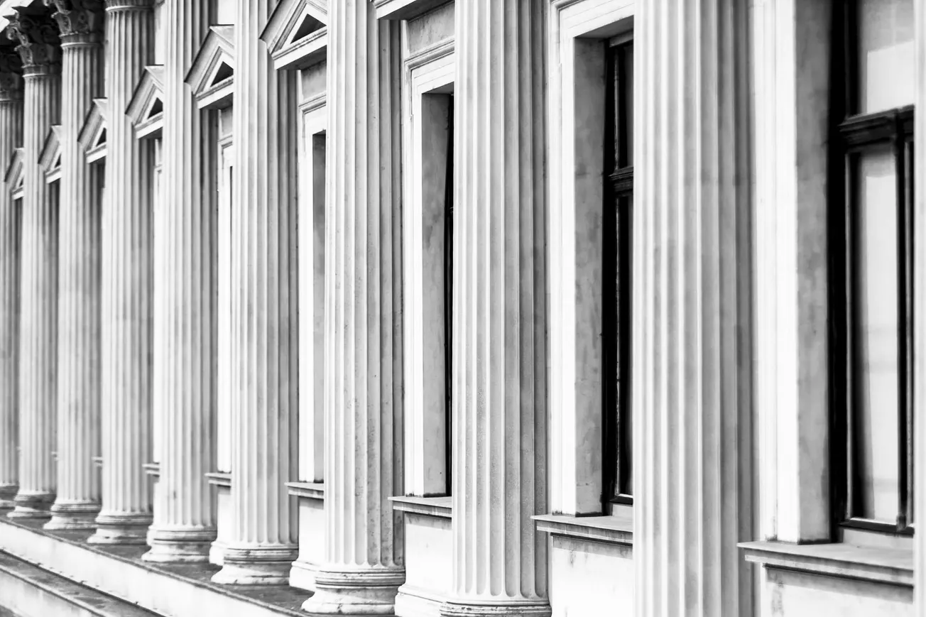 Row of classical marble columns with ornate capitals and large windows in between.