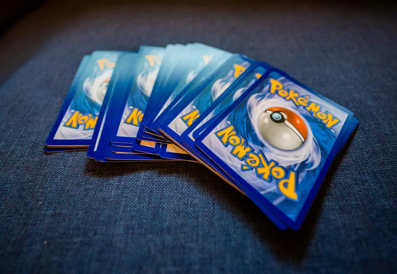 A fan of blue Pokémon cards with Pokéball designs, arranged on a dark fabric surface. The scene conveys a nostalgic and playful tone.