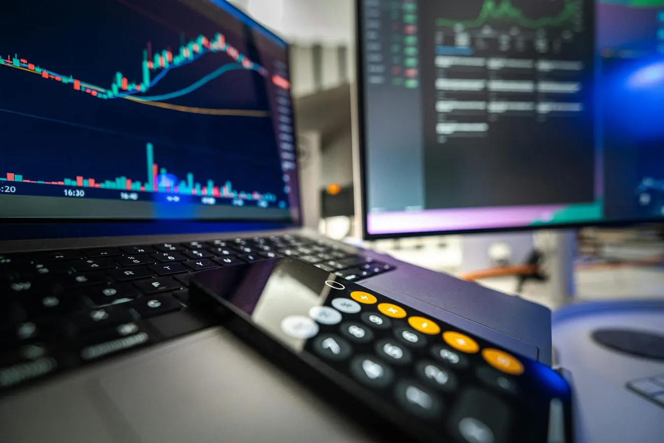 A laptop displaying a stock chart with colorful graphs, beside a calculator app on a smartphone.
