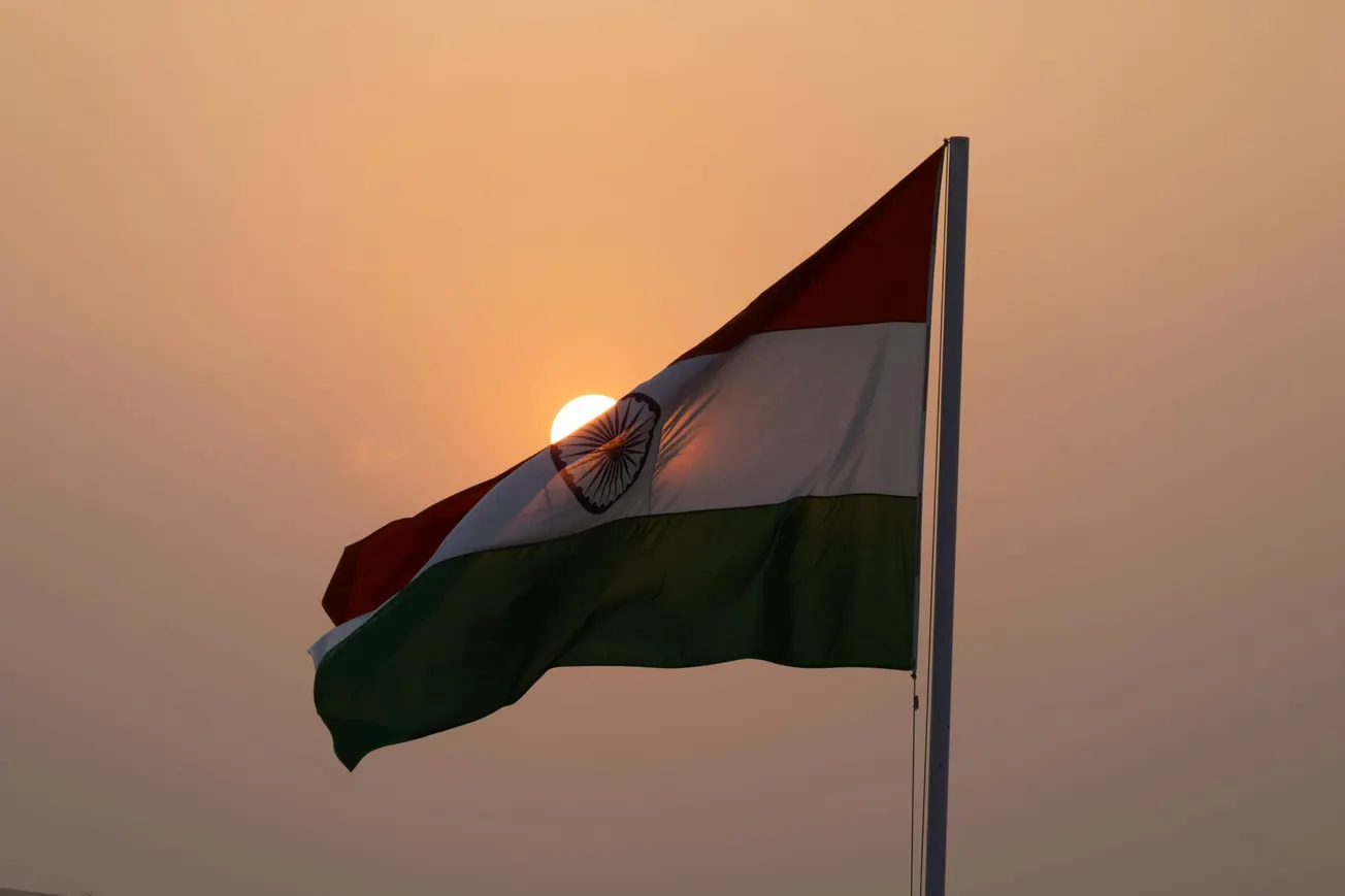 Indian flag waving in front of a setting sun, creating a dramatic silhouette. 