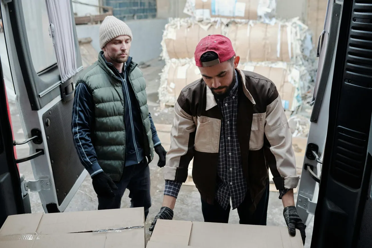 Workers unloading cardboard boxes from a delivery van for stocking retail store inventory.
