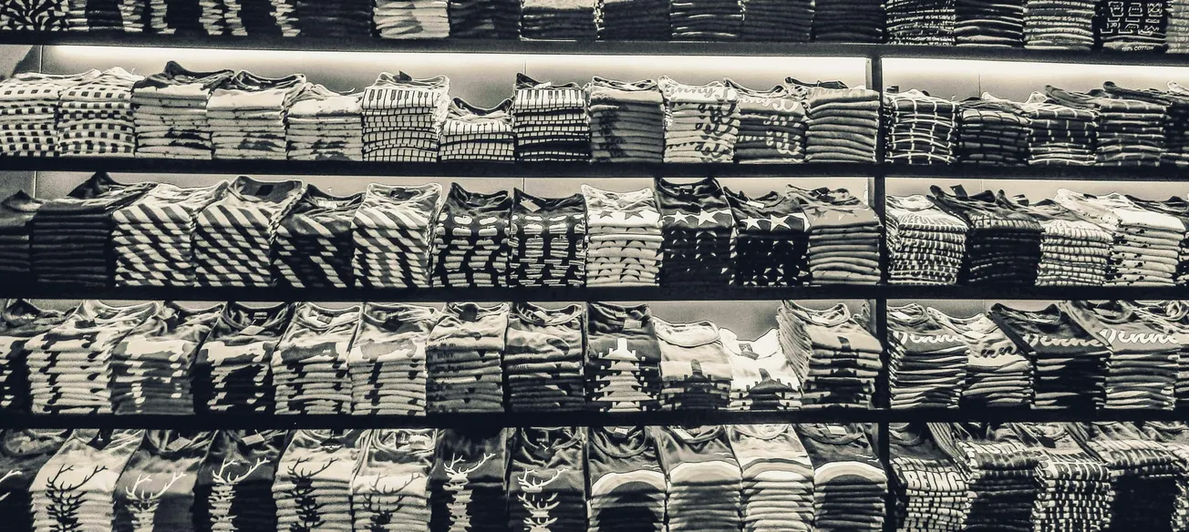 Rows of neatly folded patterned shirts on shelves in a store. The monochrome image emphasizes organization and uniformity, creating a calm, tidy atmosphere.