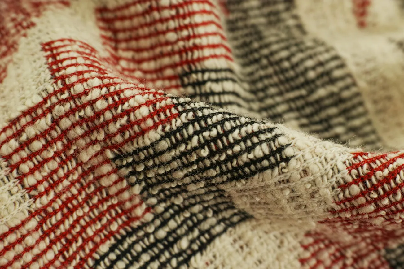 Close-up of a soft, woven fabric featuring red and black plaid patterns on an off-white background.