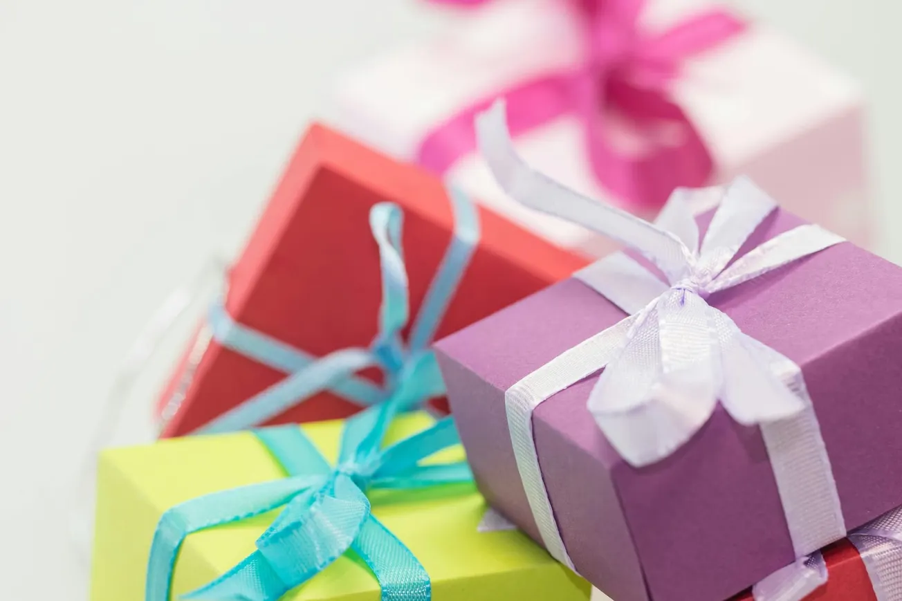 Colorful gift boxes with ribbons are stacked, featuring purple, green, pink, and red packages.