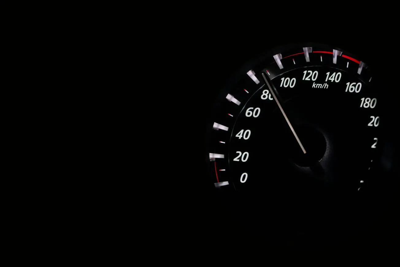 Close-up of a car speedometer in low light, showing 90 km/h against a black background, conveying a sense of speed and focus.