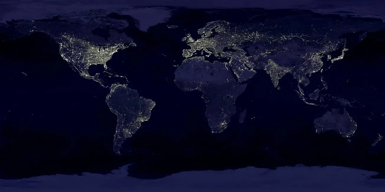 A world map at night showing city lights illuminating North America, Europe, parts of Asia and South America, highlighting urban areas against dark oceans.