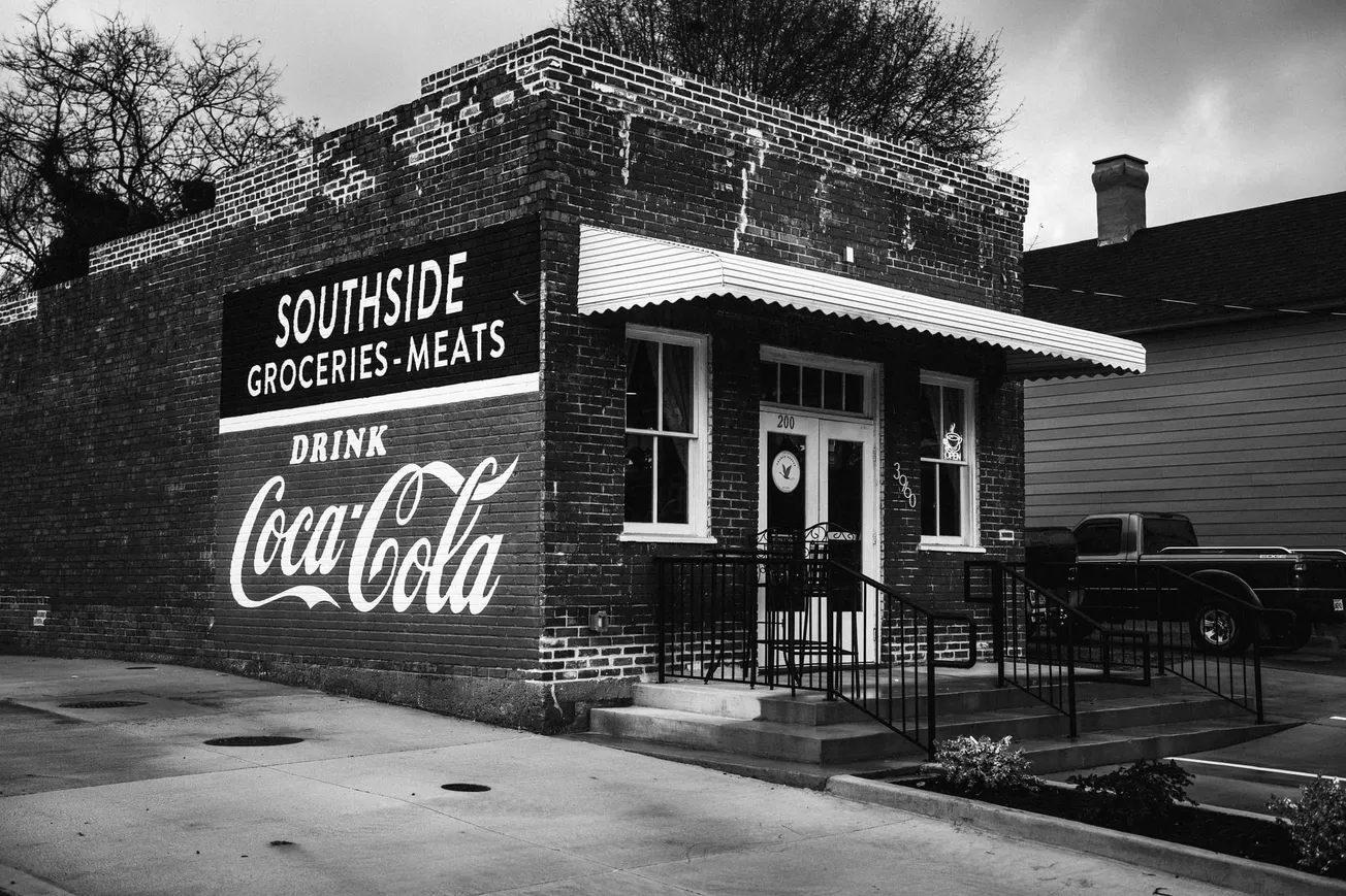 A vintage brick building labeled "SOUTHSIDE Groceries-Meats" with a large Coca-Cola sign, creating a nostalgic, historic feel. A truck is parked beside it.