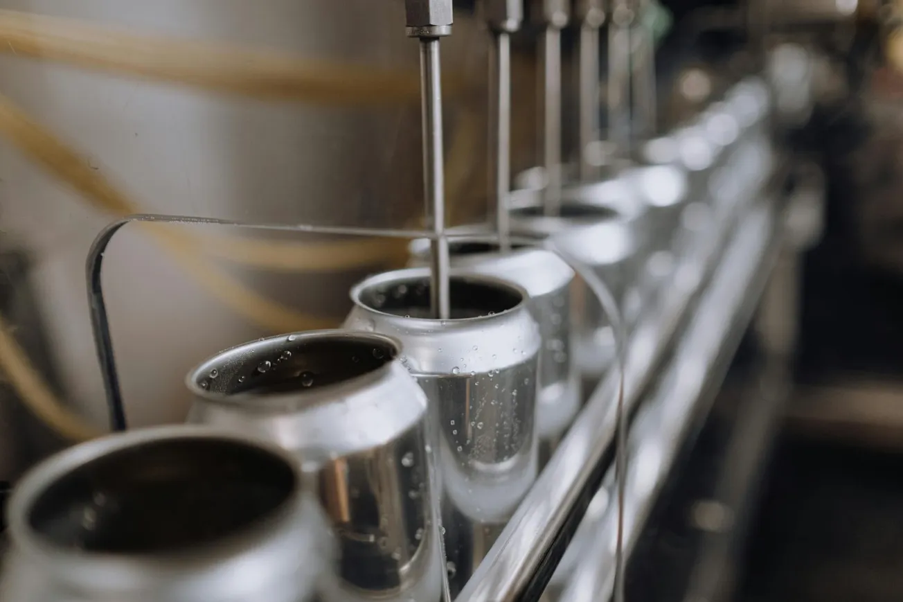 Close-up of an assembly line filling aluminum cans with liquid in a factory setting. The image conveys an industrious and efficient atmosphere.