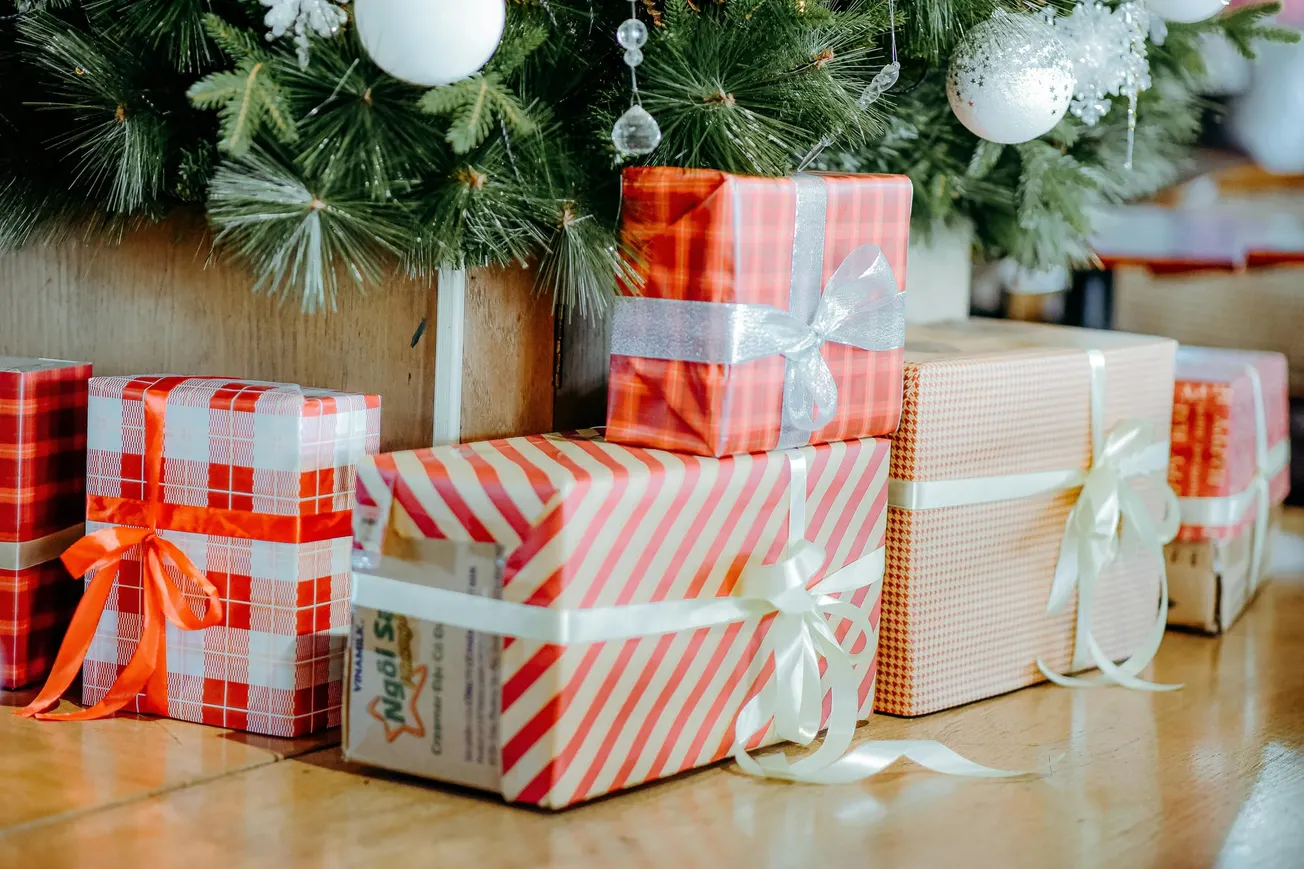 Gifts with red and white wrapping sit under a Christmas tree adorned with ornaments, conveying a festive and joyful holiday atmosphere.