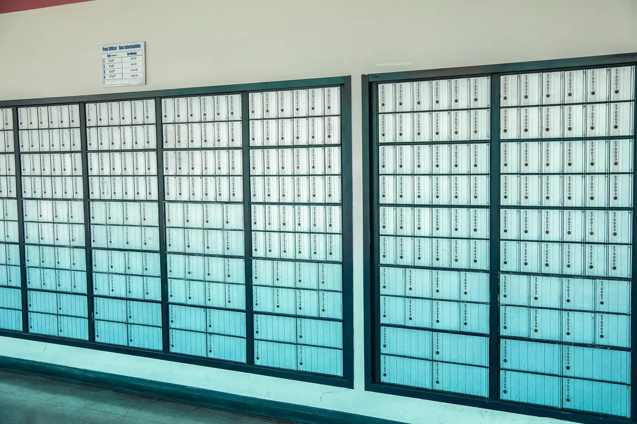 A wall of post office boxes fills the image, each with a small lock and label. The tone is orderly and institutional, conveying efficiency.