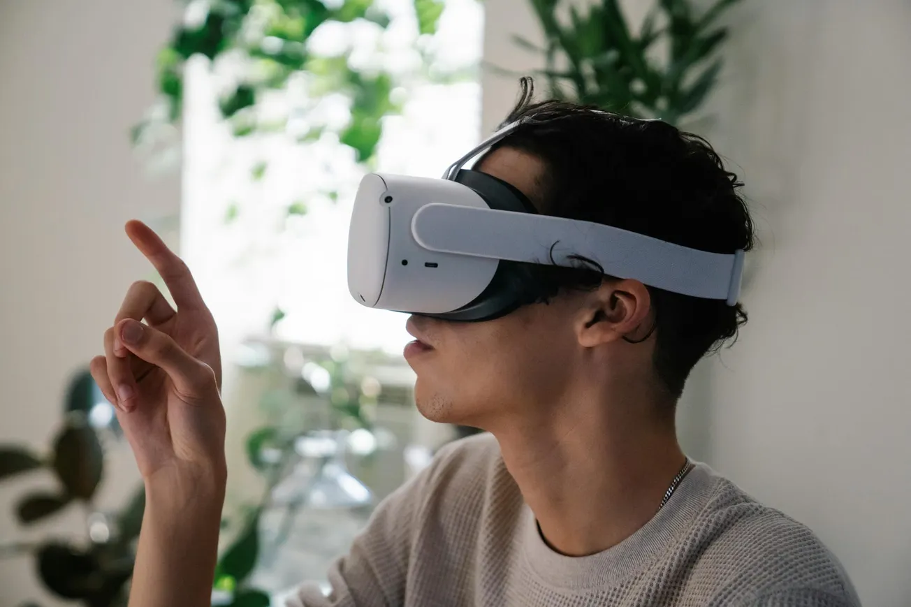 A person wearing a virtual reality headset gestures forward with one finger in an indoor setting. Soft lighting and plants create a relaxed atmosphere.