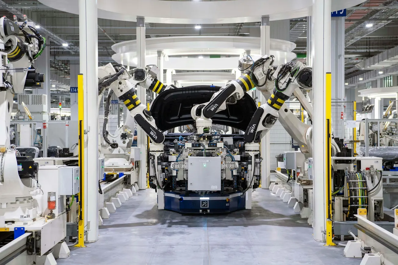 Robotic arms work on a car assembly line, with coordinated precision in a modern, well-lit factory, reflecting efficiency and technological advancement.