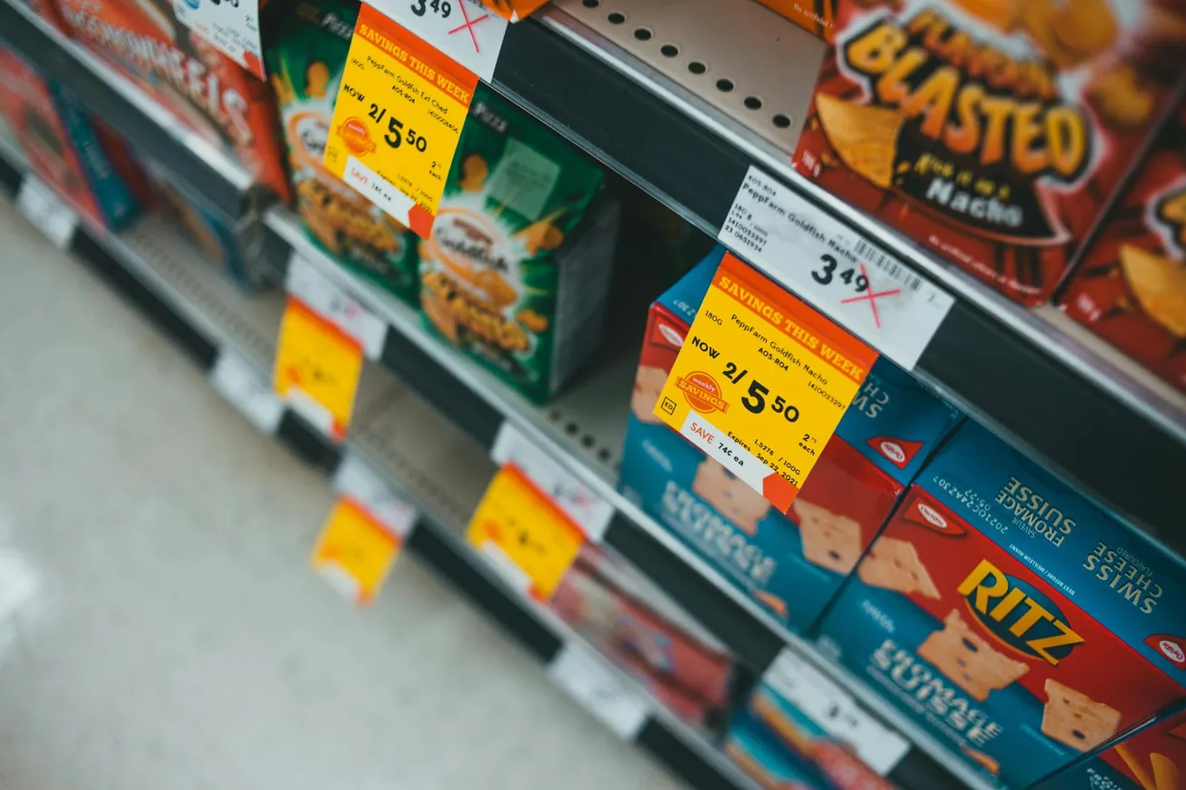 Store shelf with various snack boxes featuring brightly colored sales tags. Discounts, including "2 for $5.50," create a vibrant, enticing display.