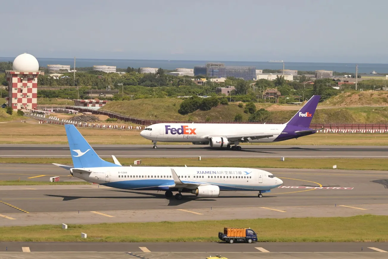 Two airplanes on a sunny airport runway: a FedEx cargo plane in the background and a Xiamen Airlines passenger jet in the foreground.