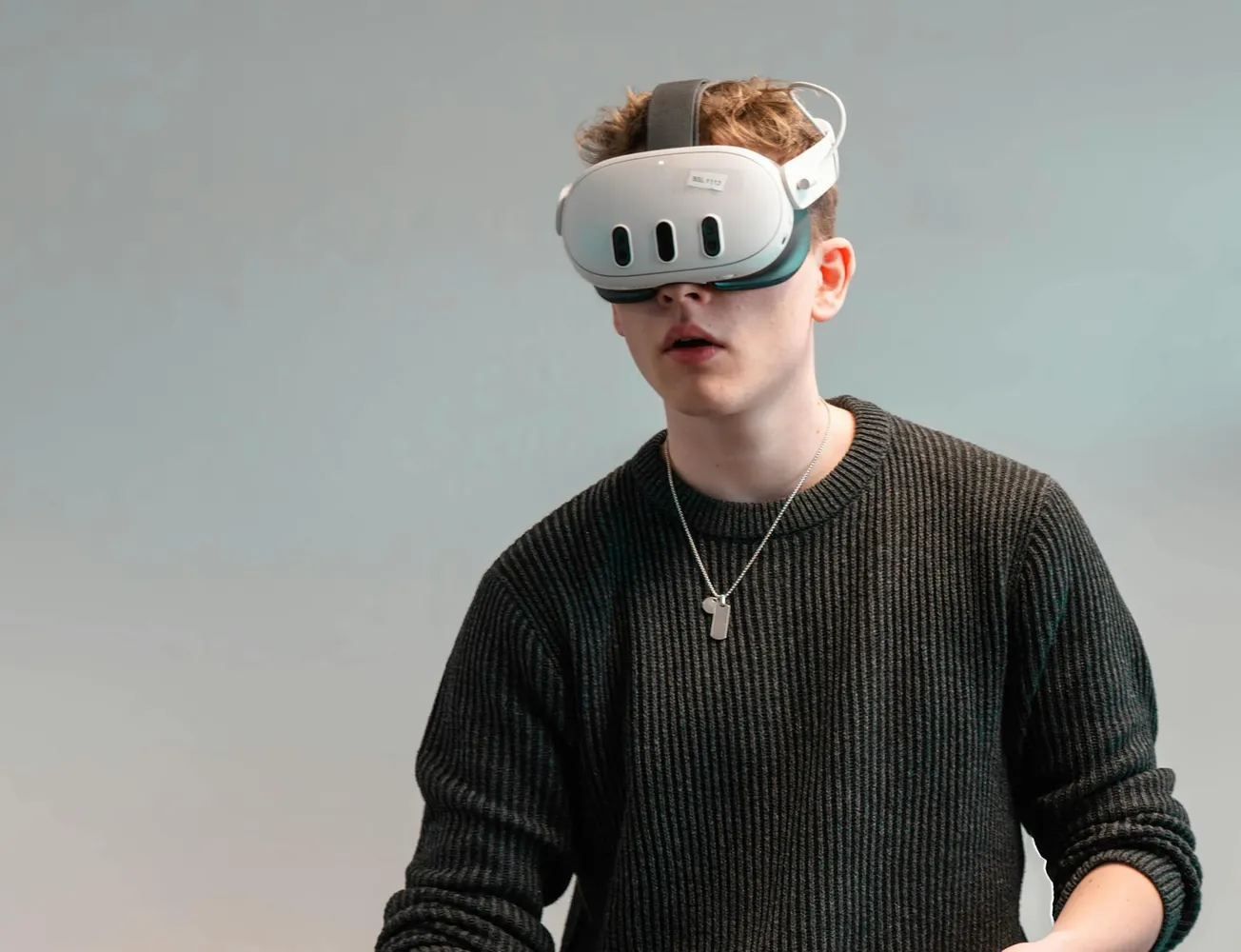 Young person wearing a virtual reality headset, dressed in a dark sweater. They appear focused and engaged in a VR experience against a plain background.