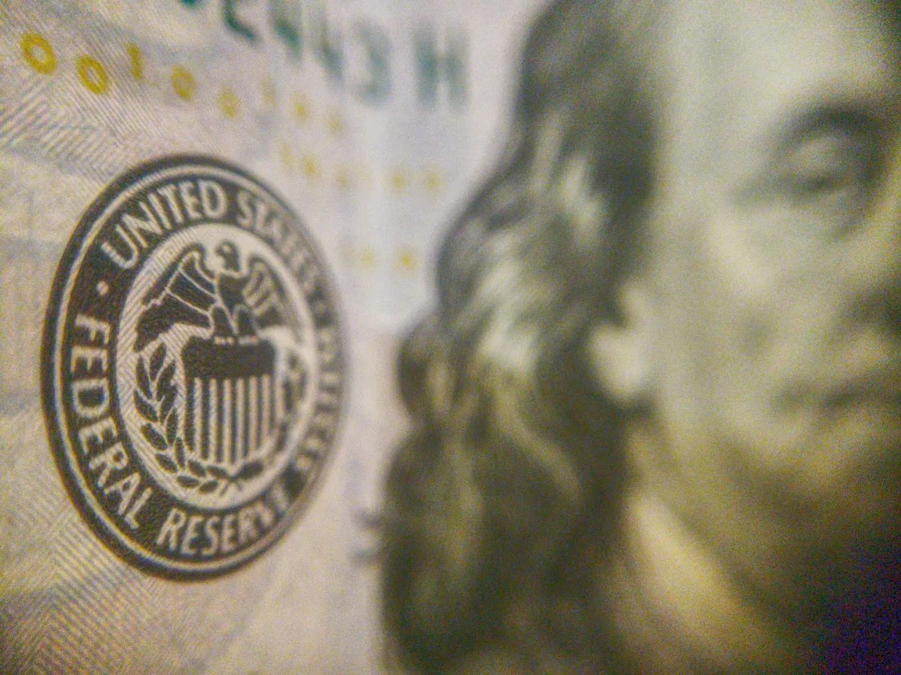 Close-up of a U.S. hundred-dollar bill showing the Federal Reserve emblem and the blurred face of Benjamin Franklin, emphasizing security features.