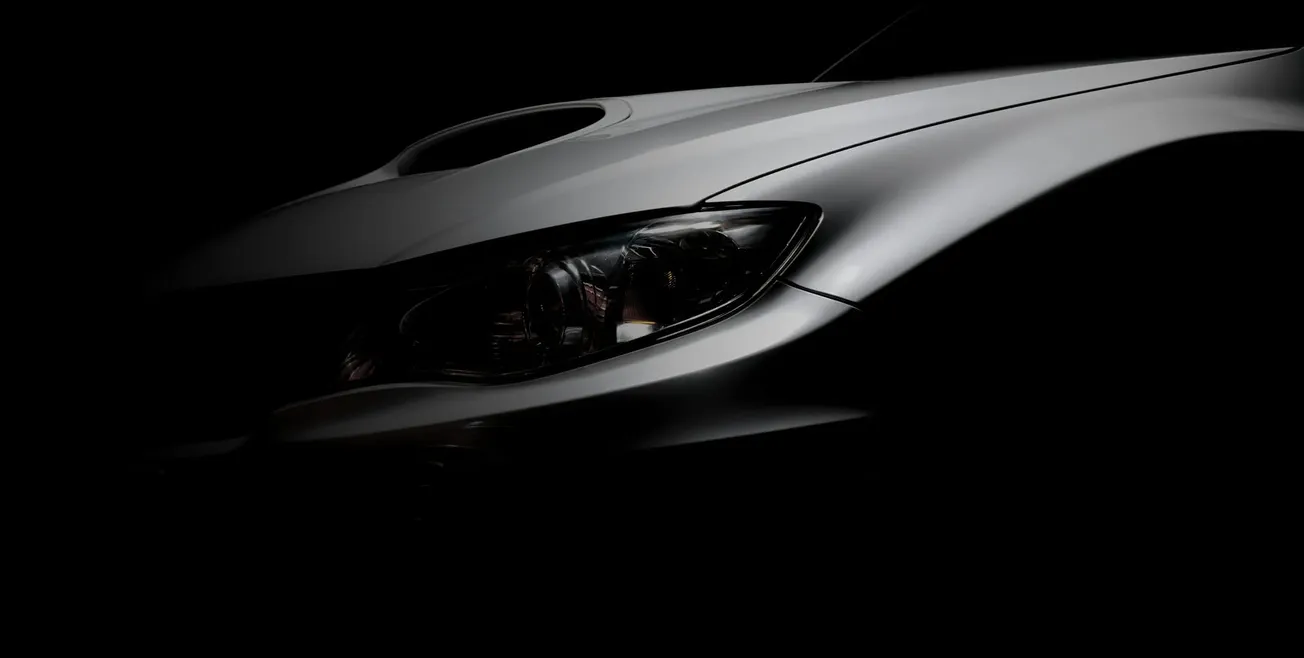 Close-up of a sleek car front in shadow, showing its glossy silver hood and sharp headlight. The lighting adds a mysterious, sophisticated tone.