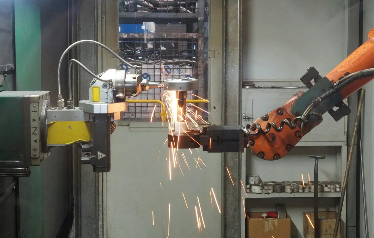 Industrial robotic arm welding metal parts in a factory, emitting bright sparks. The scene conveys precision and advanced manufacturing technology.