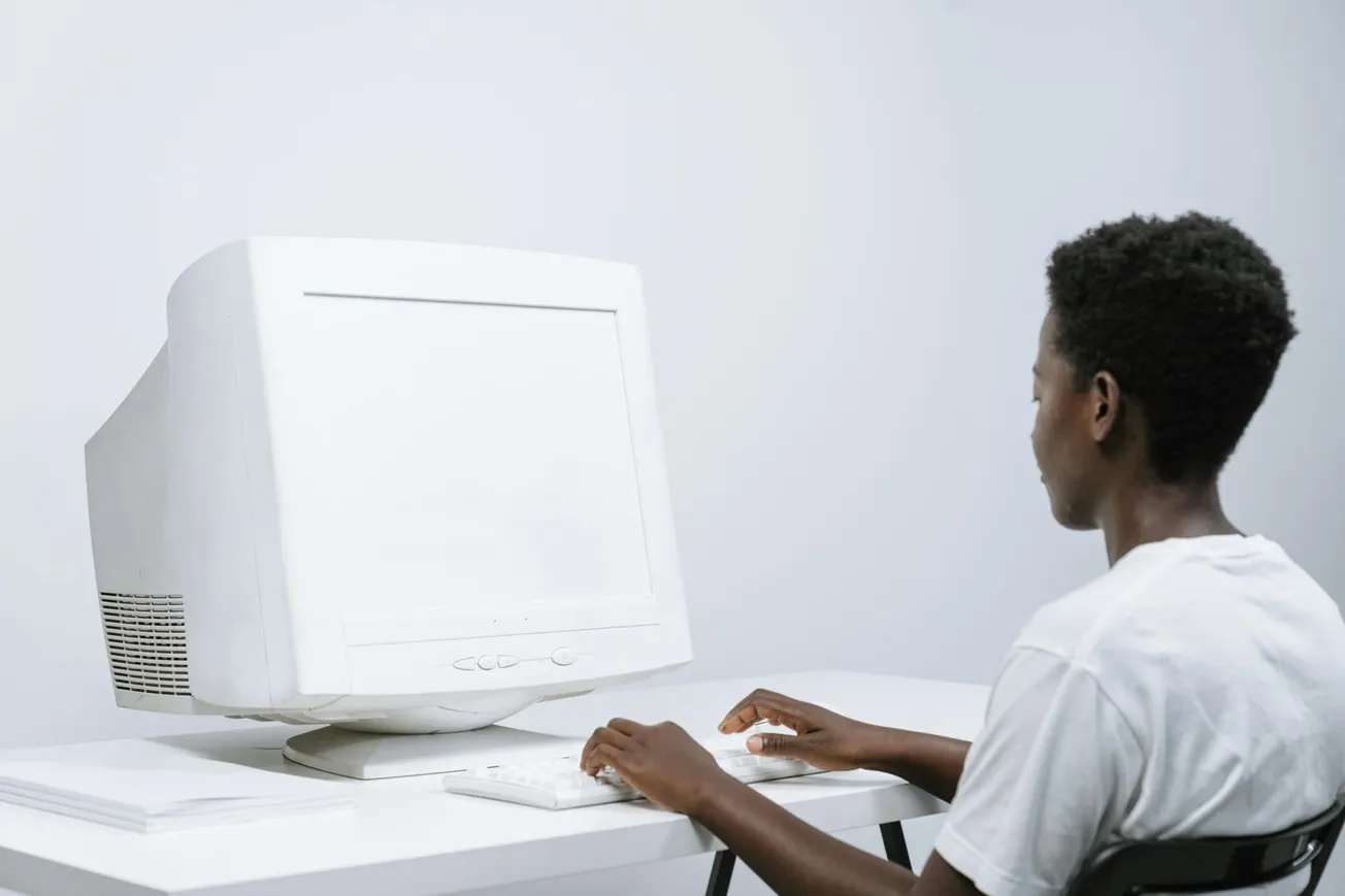 A person in a white T-shirt sits at a desk using a vintage CRT monitor and keyboard, exuding a nostalgic, retro tech vibe in a minimalist setting.