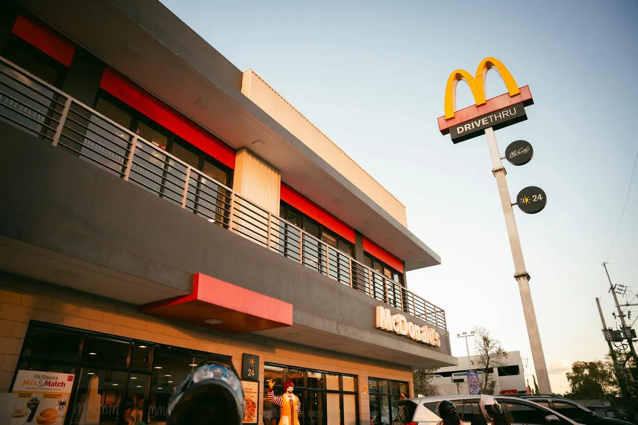A McDonald's restaurant exterior during sunset, showcasing the iconic yellow arches and a drive-thru sign.