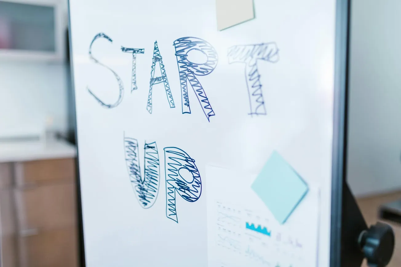 Whiteboard with "START UP" written in bold, blue letters. Sticky notes and charts are attached, creating a dynamic and innovative office atmosphere.
